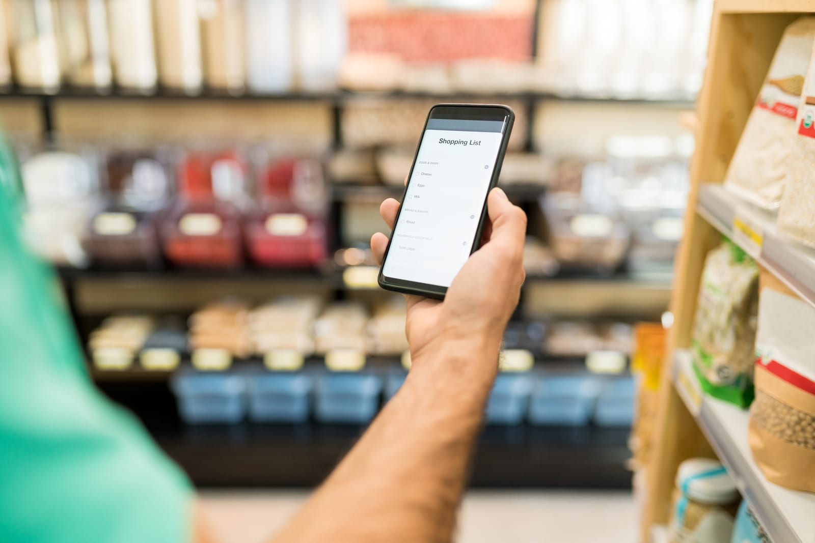 Hombre consultando la lista de la compra en su móvil en el pasillo de un supermercado